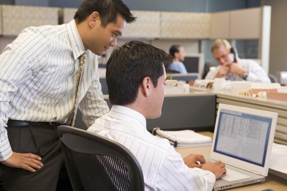 Two businessmen in cubicle looking at laptop